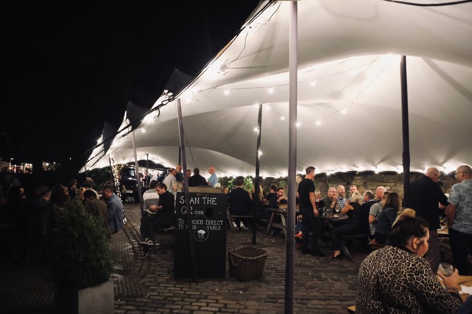 Crowds at the Annual Beer and Cider Festival under a lit marquee at night.